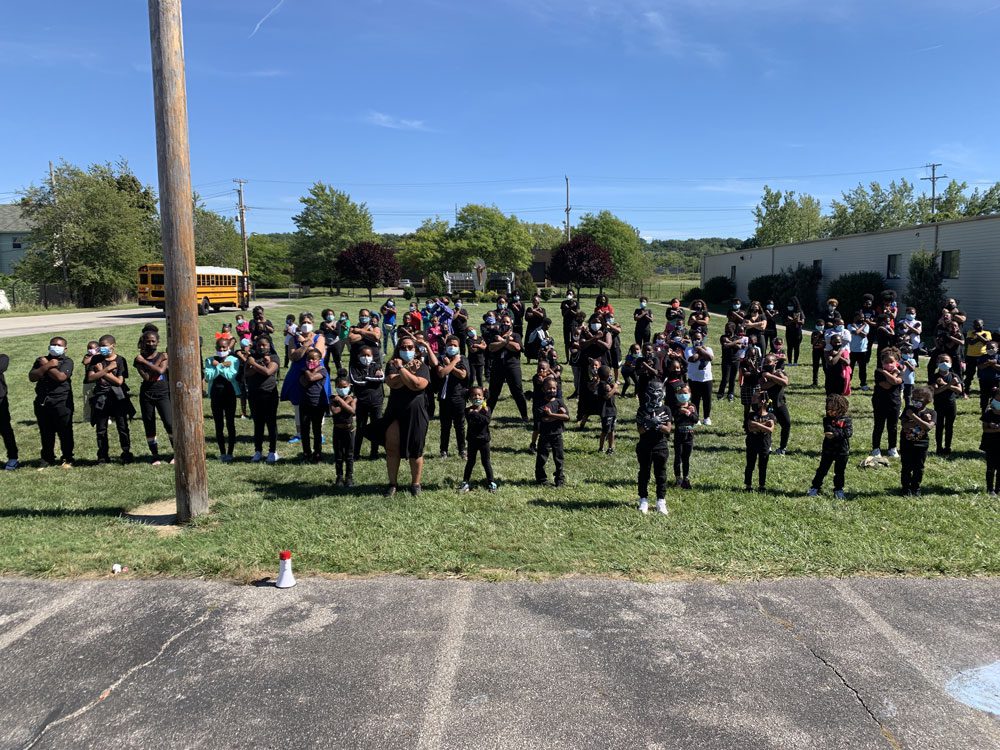 Large group of adults and children posing with crossed arms outdoors.