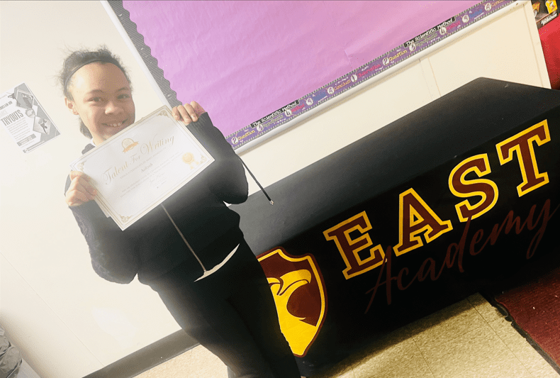 Student smiling, holding a "Talent For Writing" certificate.