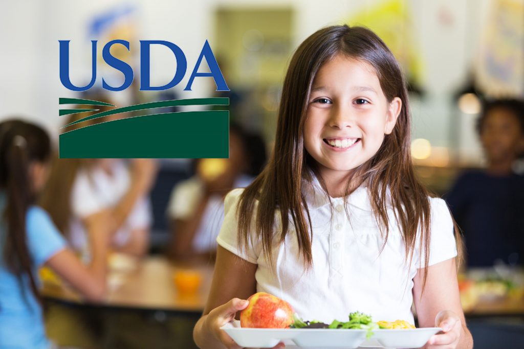 Smiling child holding a tray with an apple and salad, with USDA logo.