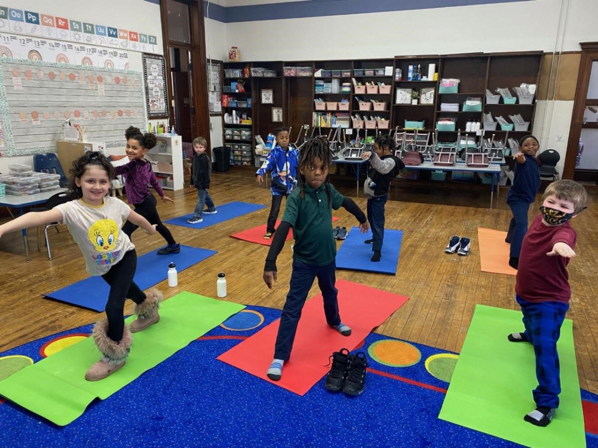 Children in a classroom doing yoga poses on colorful mats.