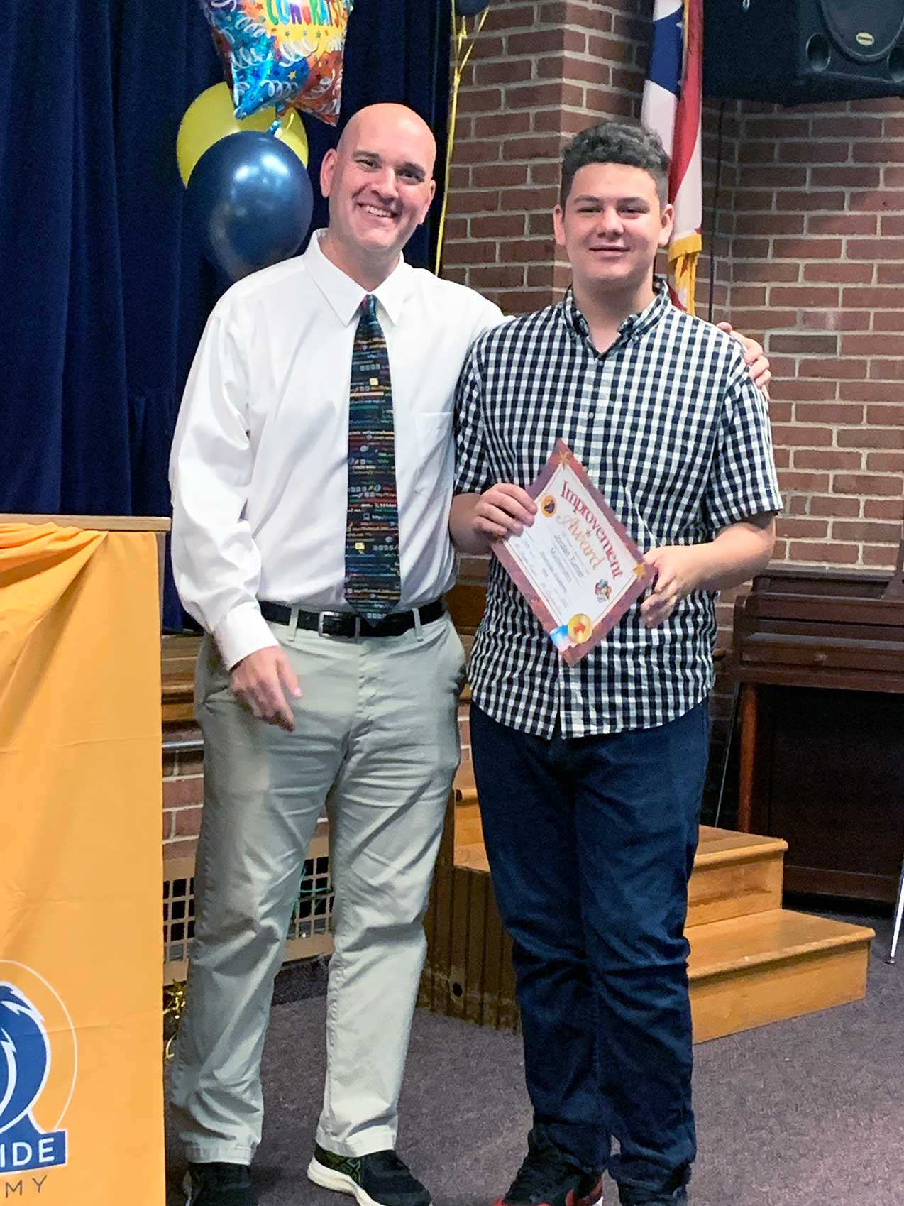 Adult and child smiling, child holding an award certificate.
