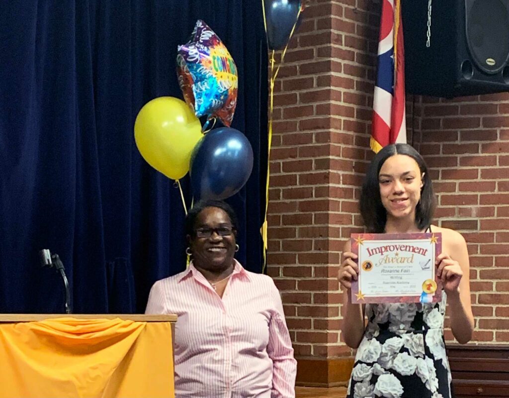 Adult and child with award certificate and balloons.
