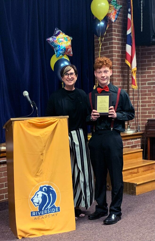 Adult and child smiling, child holding an award plaque.