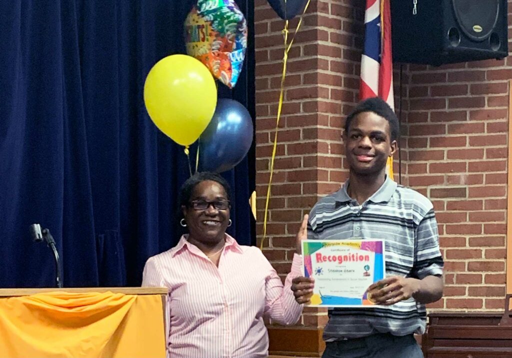 Adult and child smiling, child holds certificate.