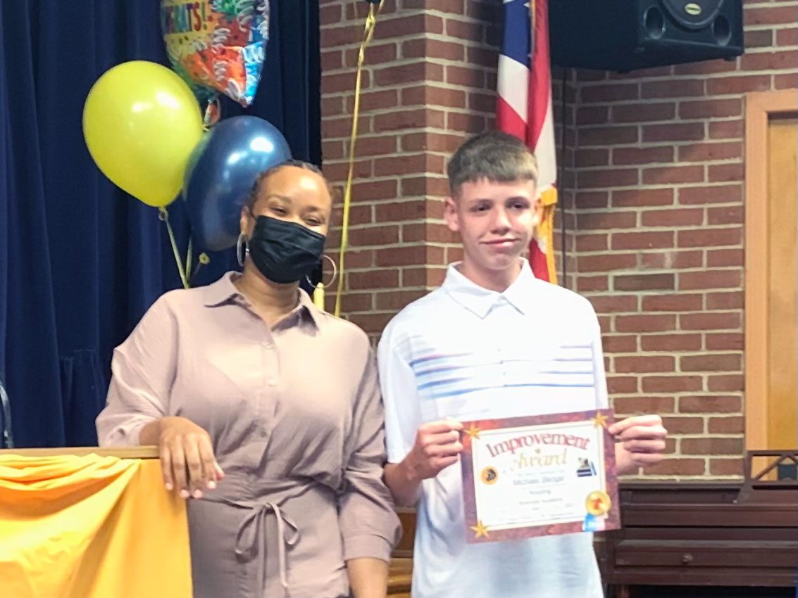 Adult and child pose with an "Improvement Award" certificate.