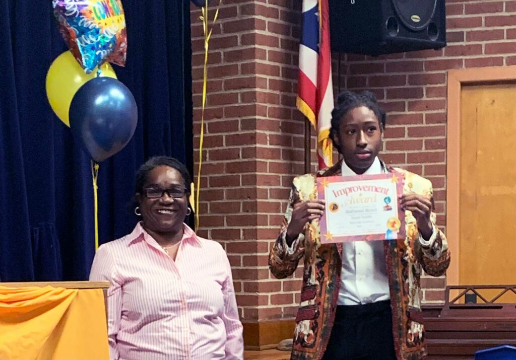 Adult and child smiling, child holds "Improvement Award" certificate.