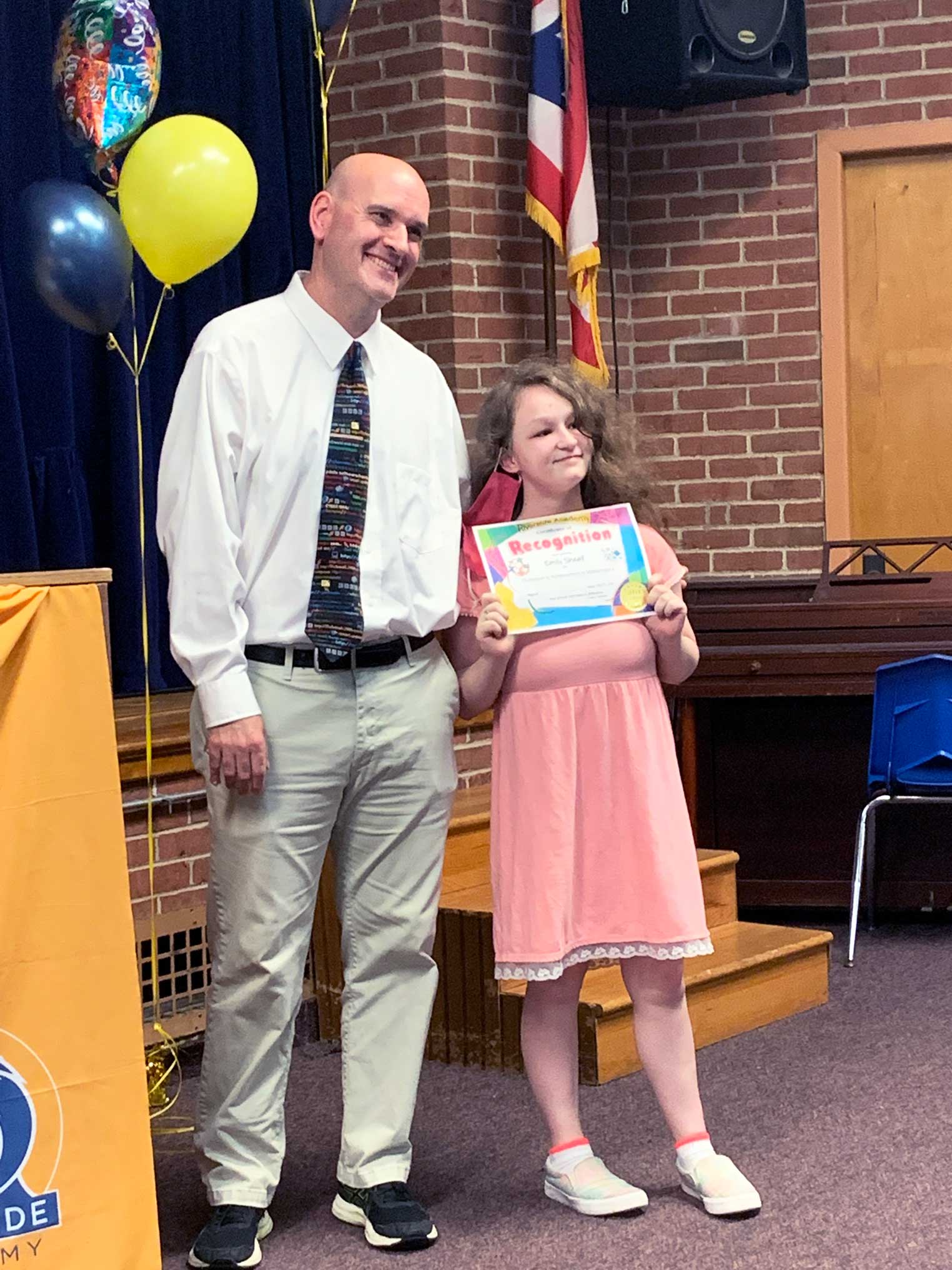 Adult and child smiling, child holding a "Recognition" certificate.