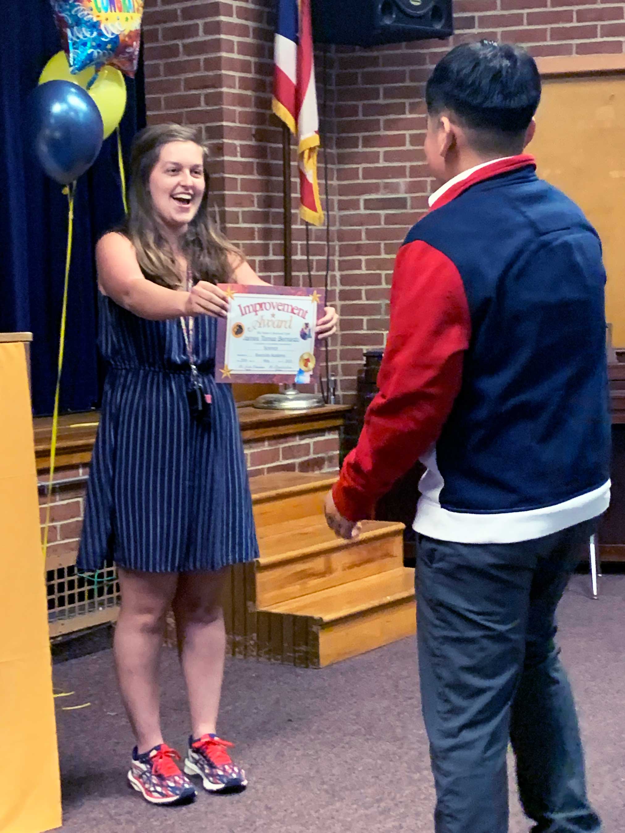 Adult presents "Improvement Award" certificate to a child.