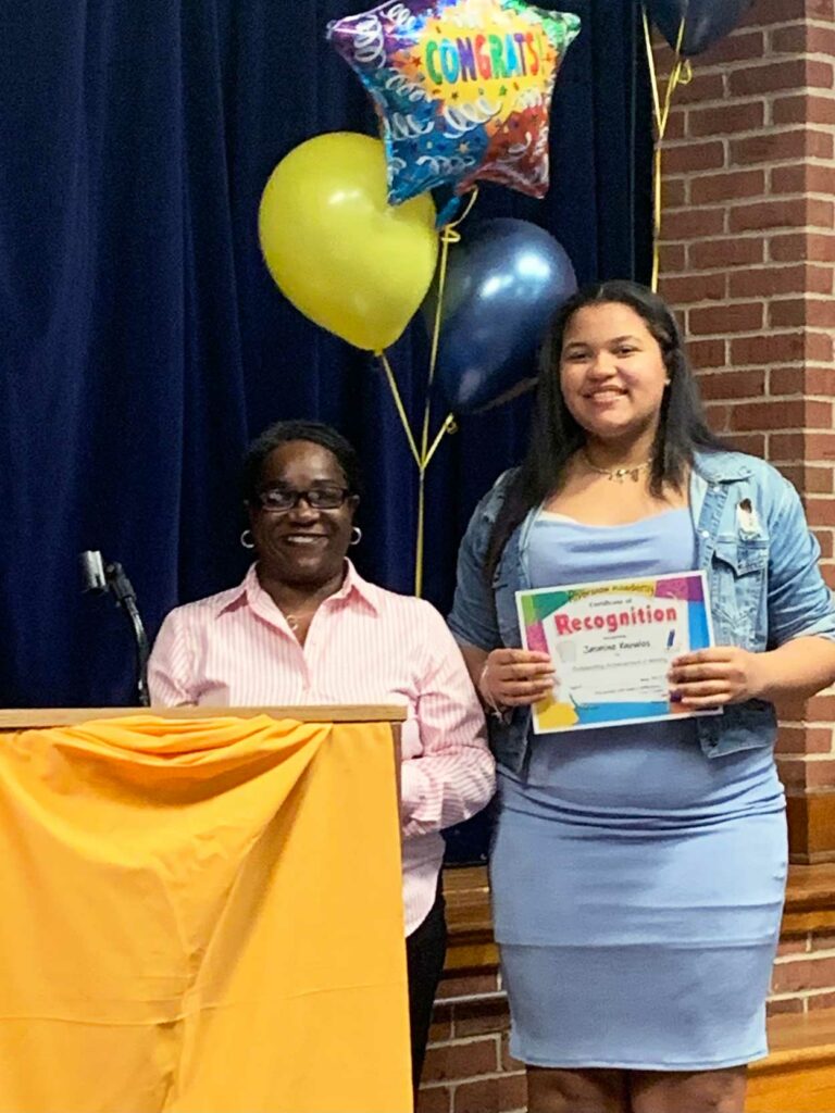 Adult and young adult holding a recognition certificate with balloons.