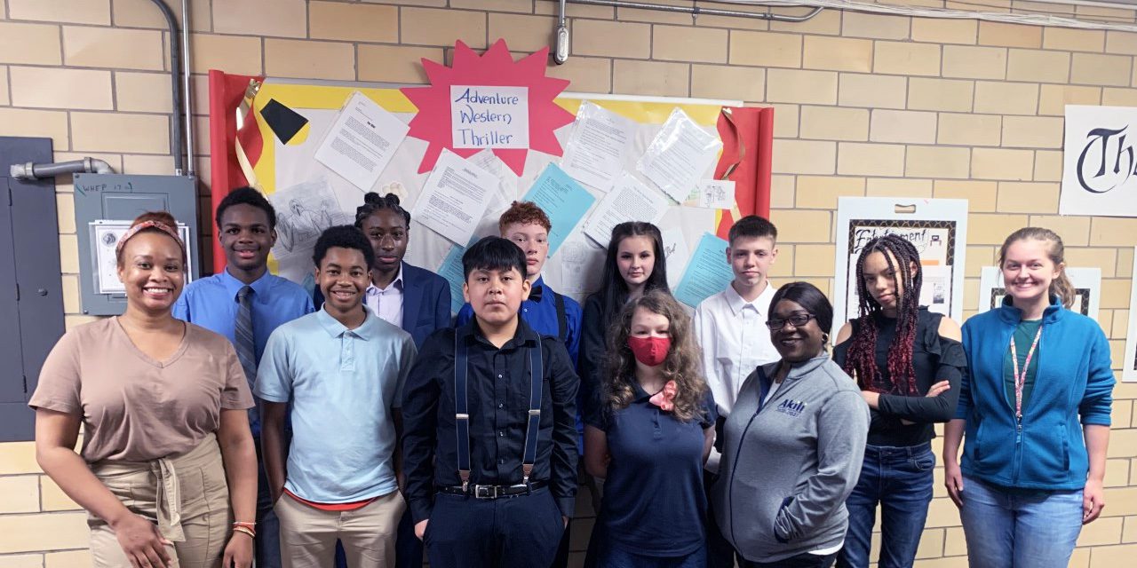 Group of adults and children smiling in front of a bulletin board.