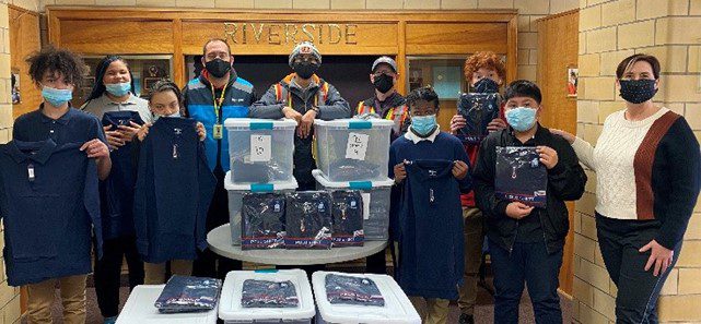 Adults and children with donated navy blue shirts and storage bins.