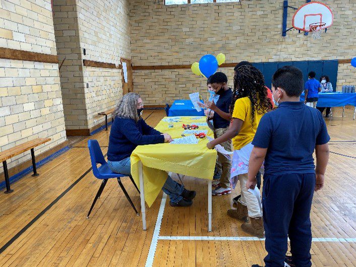Adult at table with children in gymnasium.
