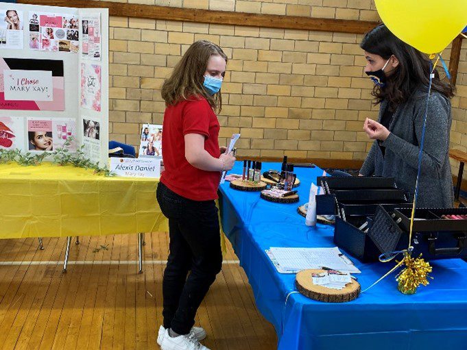 Adult and child at a table with cosmetics and promotional display.