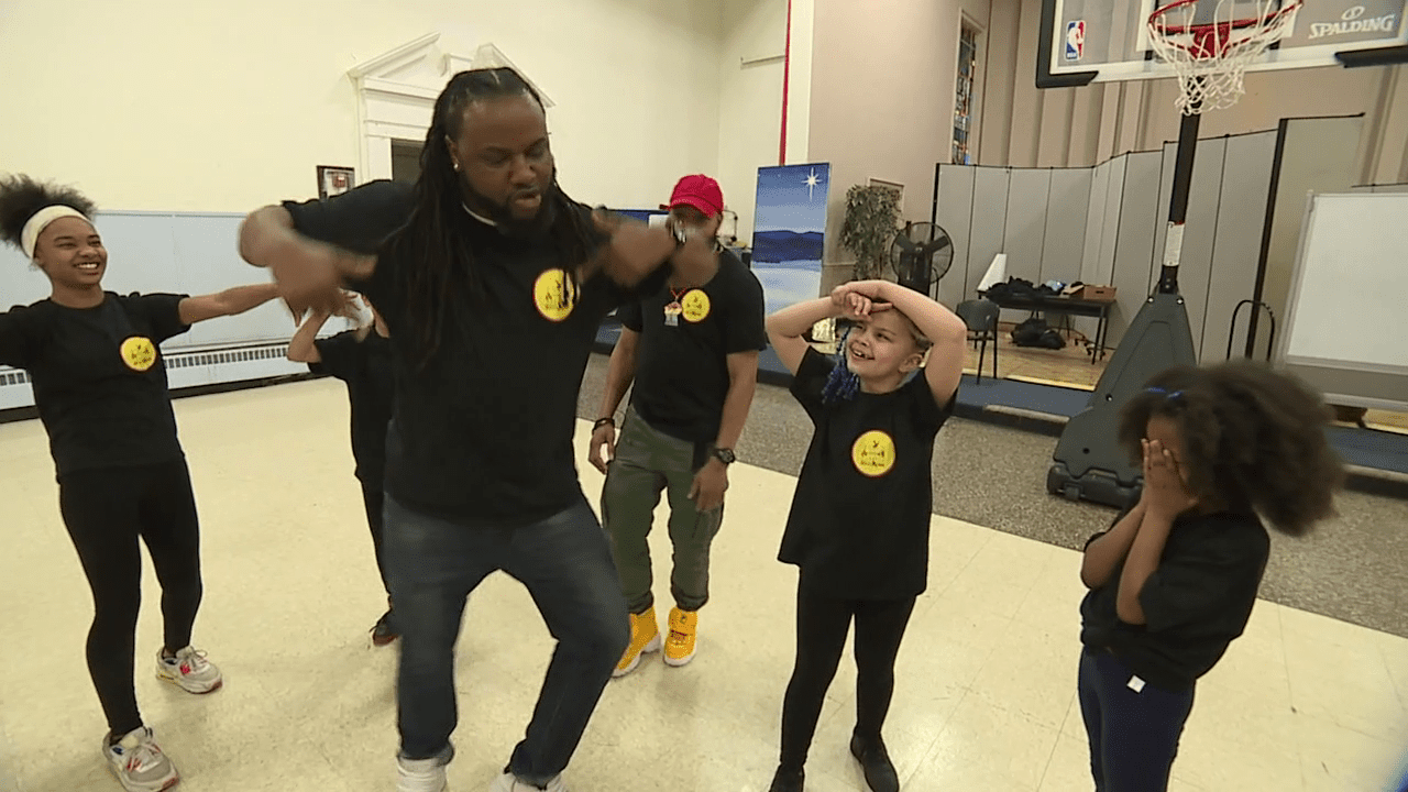 Adults and children in black shirts dancing indoors.