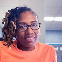 Smiling adult with dreadlocks and glasses.