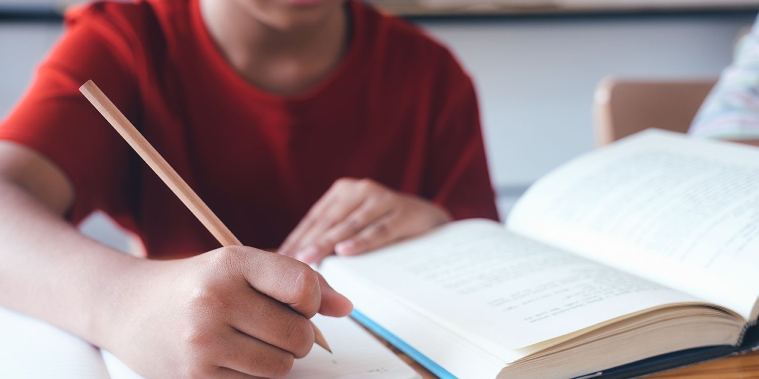 Child writing with a pencil next to an open book.