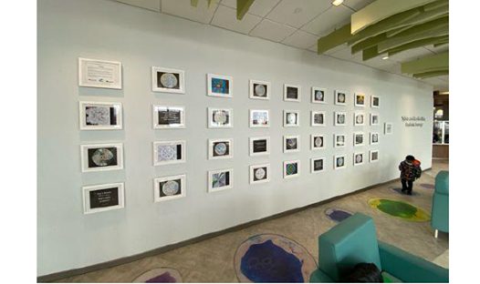 Wall with many framed artworks and awards, child standing nearby.