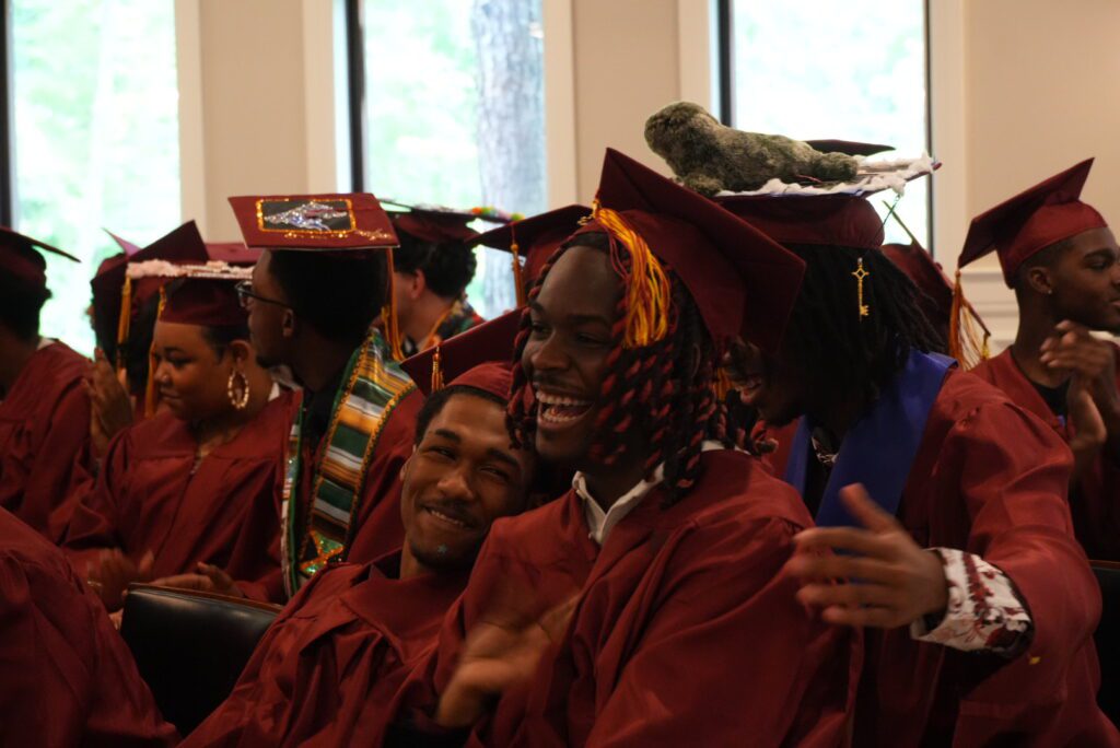 Graduates in maroon caps and gowns laughing and smiling.
