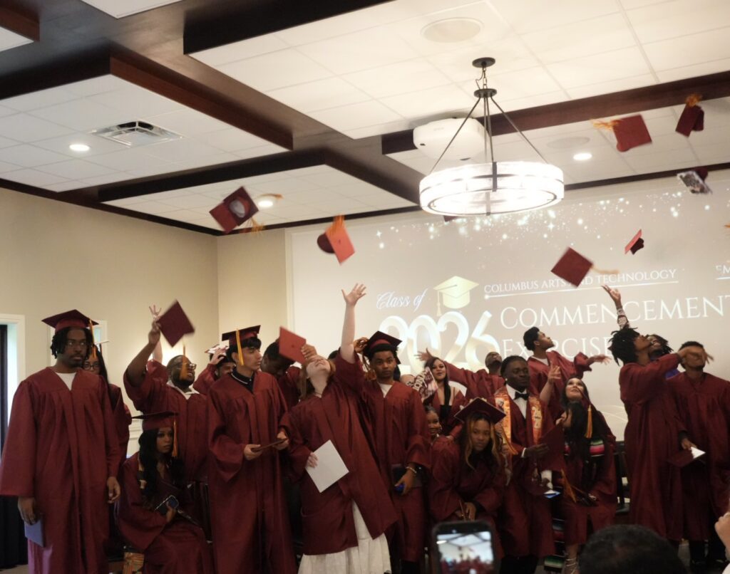 Young adults in maroon gowns throwing graduation caps in the air.