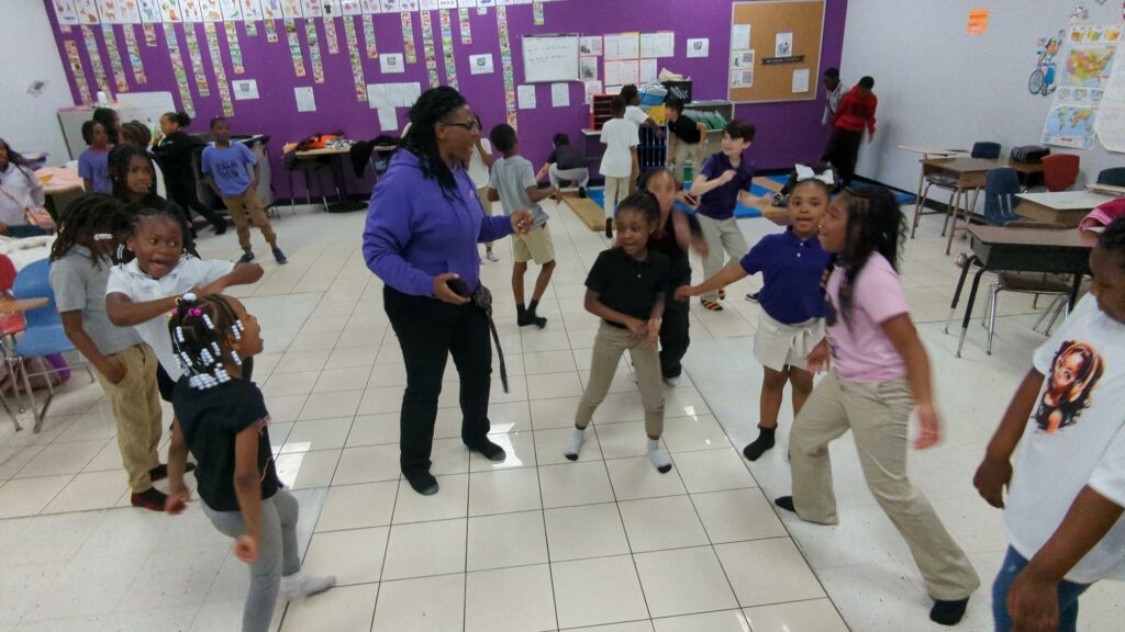 Adult and children dancing in a classroom.