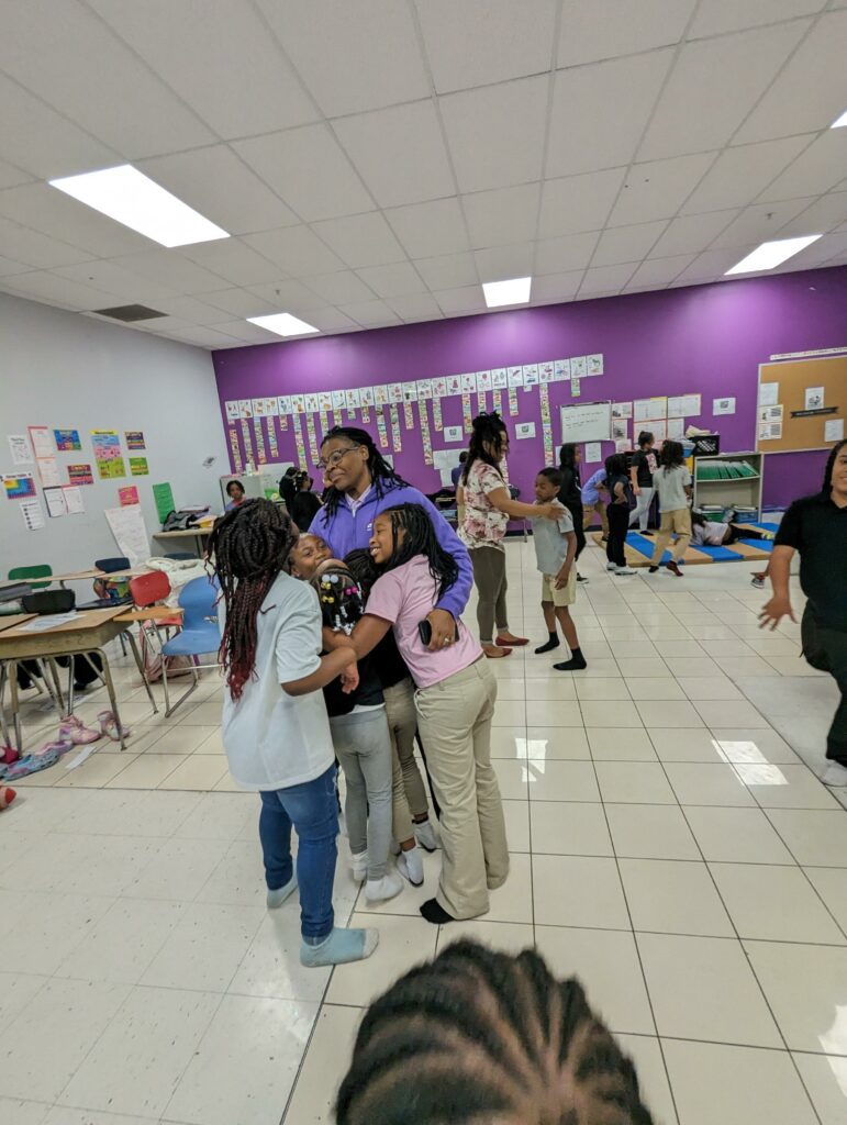 Adult hugging three children in a classroom.