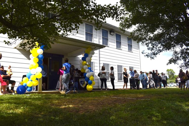People gathered outside a building with a blue and yellow balloon arch.