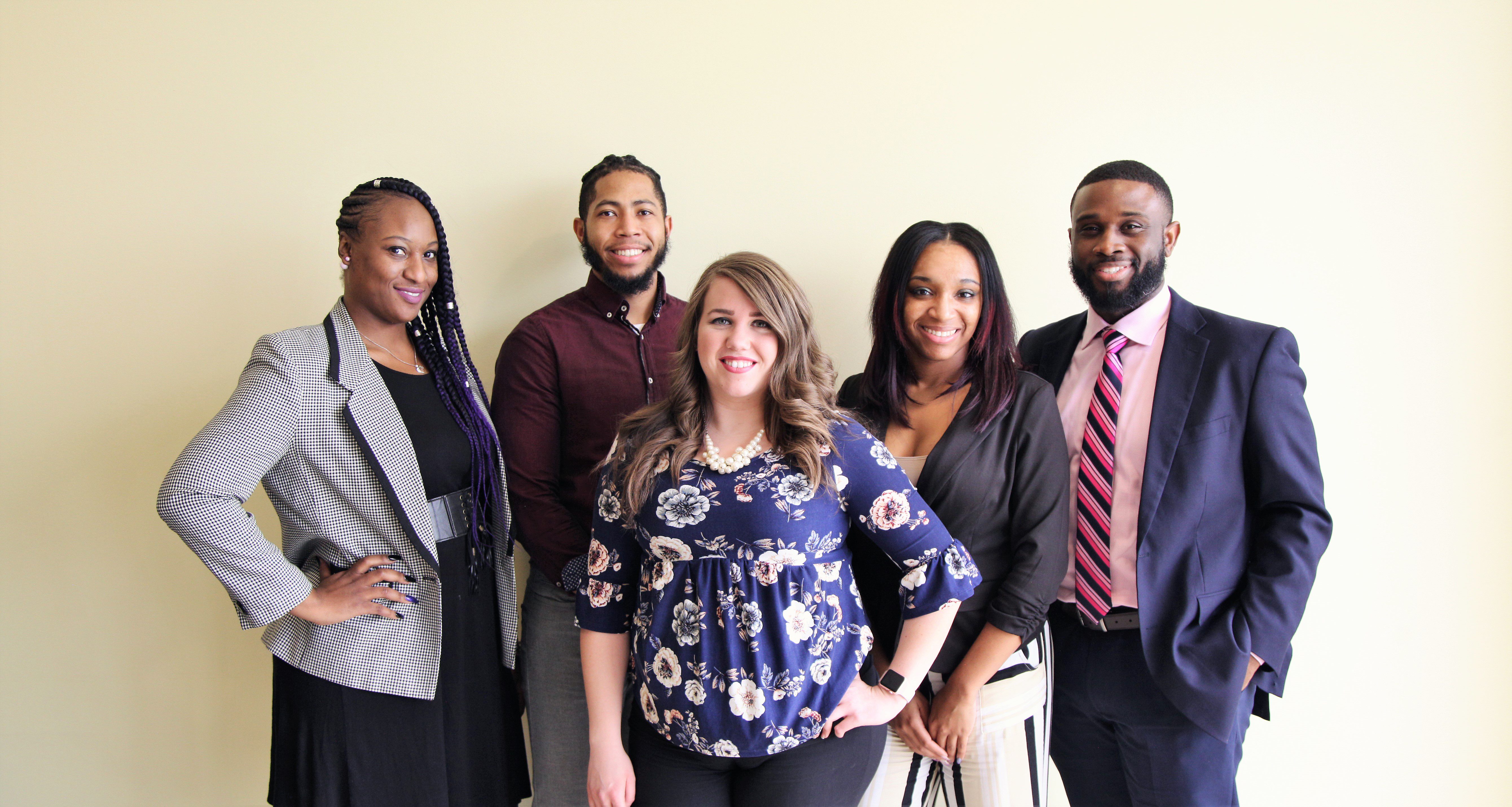 Five smiling adults posing for a group photo.