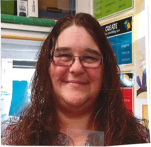 Smiling adult with long hair and glasses.