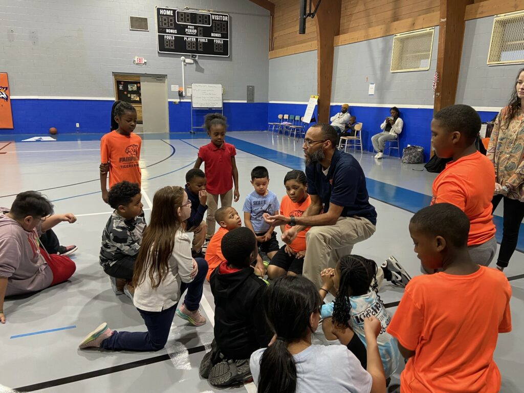 Adult speaking to children on a basketball court.