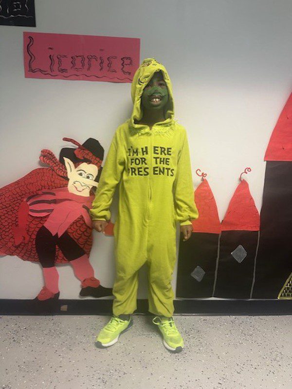 Child in green costume and face paint stands by wall decorations.