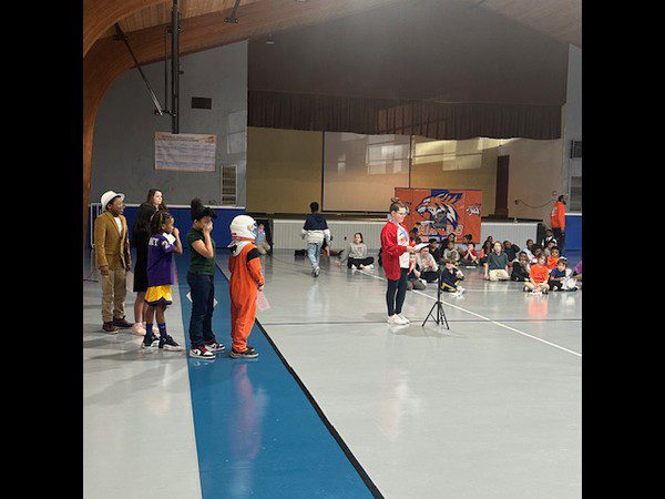 Children in costumes stand in a line on a gymnasium floor.