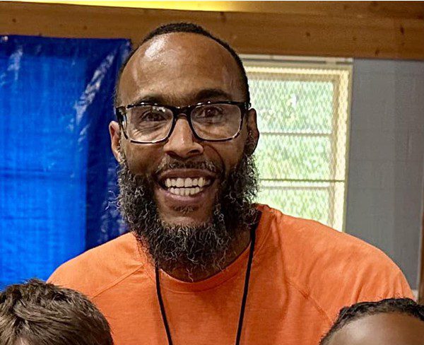 Smiling adult with glasses and beard, with children in foreground.