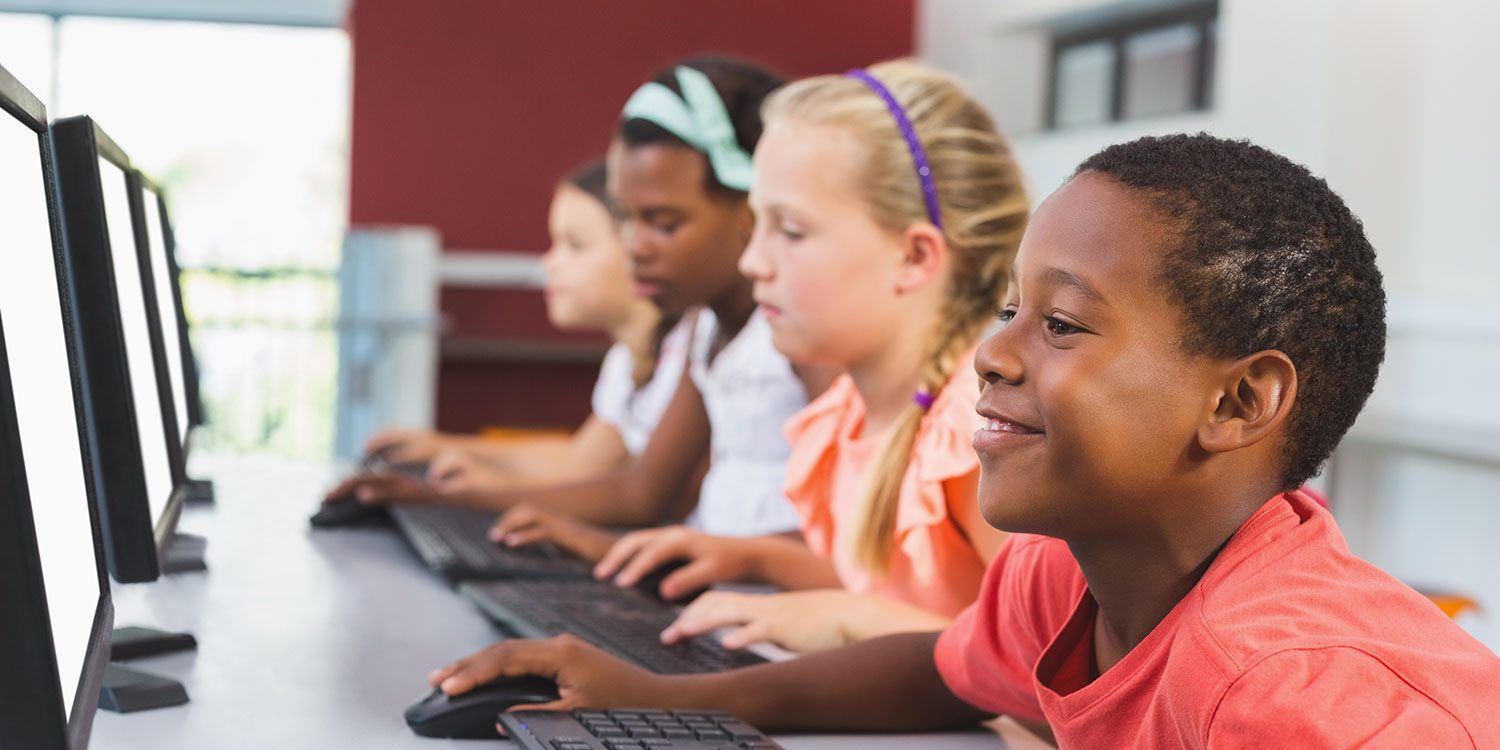 Children in a classroom using computers with blank screens.