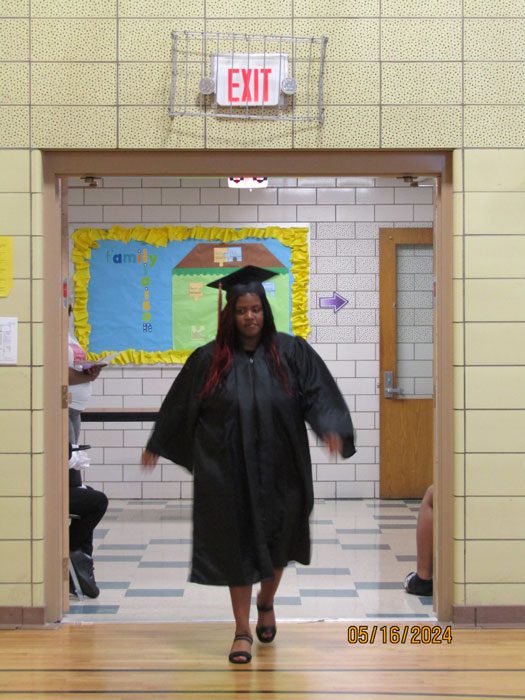 Adult in graduation gown and cap walking through a doorway.