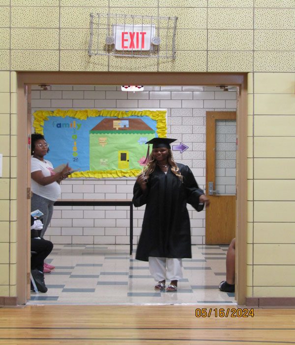 Adult in graduation gown and cap walking through a doorway.