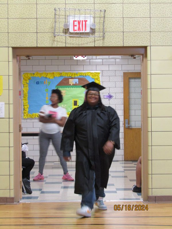 Adult in graduation cap and gown walks through doorway.