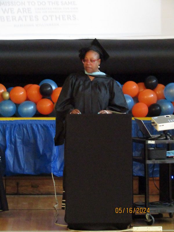 Adult in graduation gown and cap at podium.