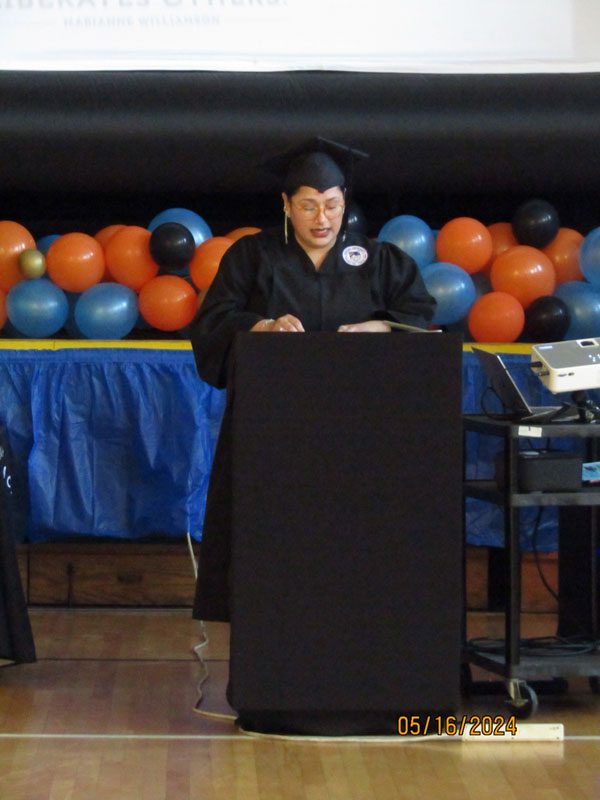 Adult in graduation attire speaking at a podium.