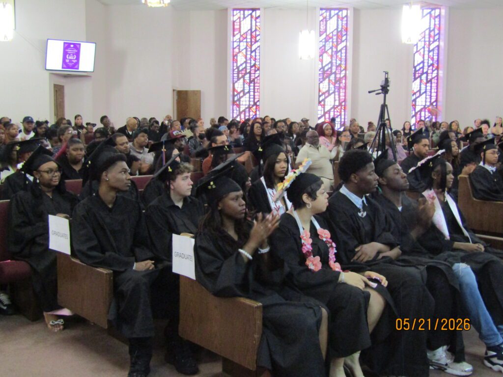 Graduates in caps and gowns seated in pews during a ceremony.