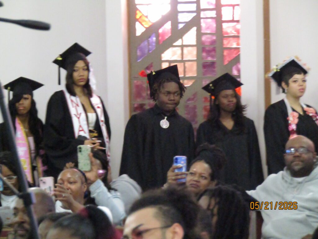 Young adults in graduation caps and gowns with attendees taking photos.