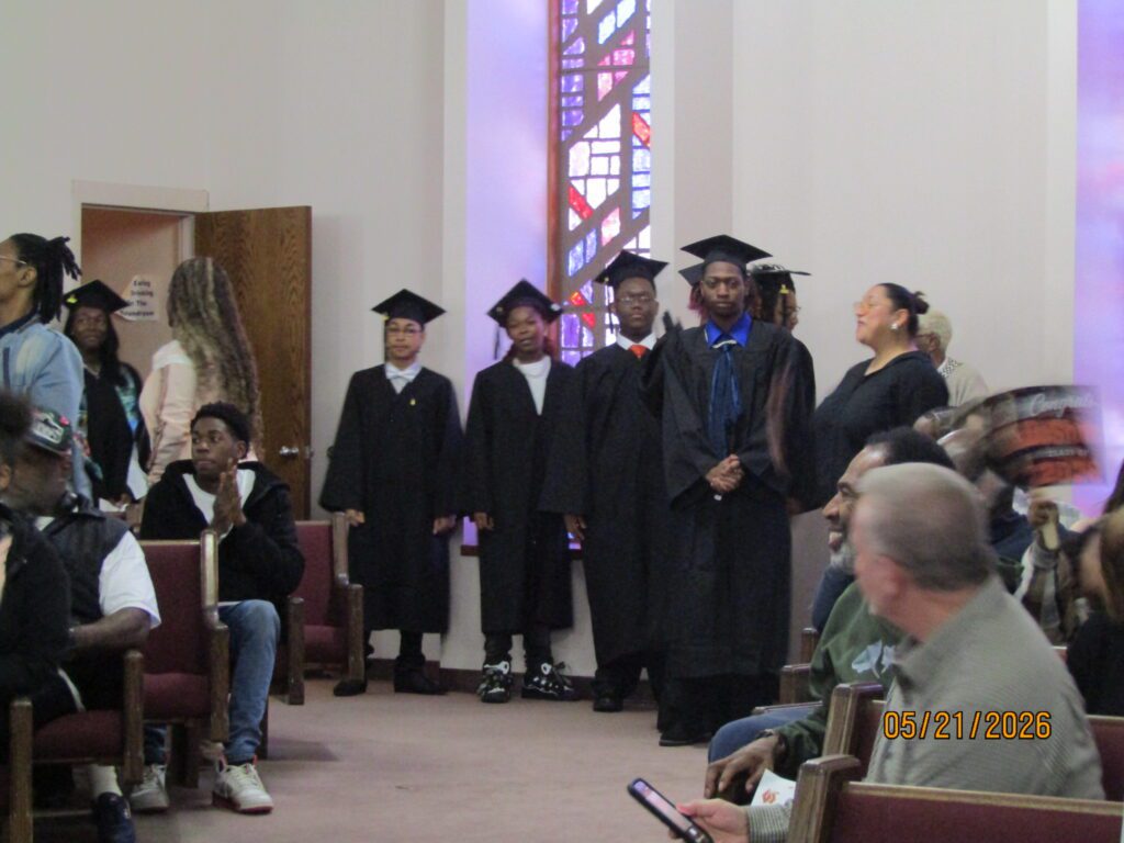 Young adults in graduation caps and gowns stand in a hall.