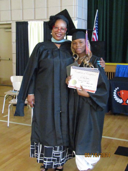 Two adults in graduation attire, one holding a certificate.