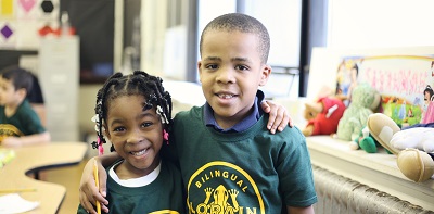 Two smiling children in green shirts in a classroom.