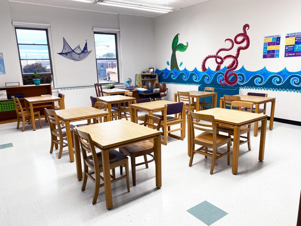 Classroom with wooden tables, chairs, and an ocean mural.