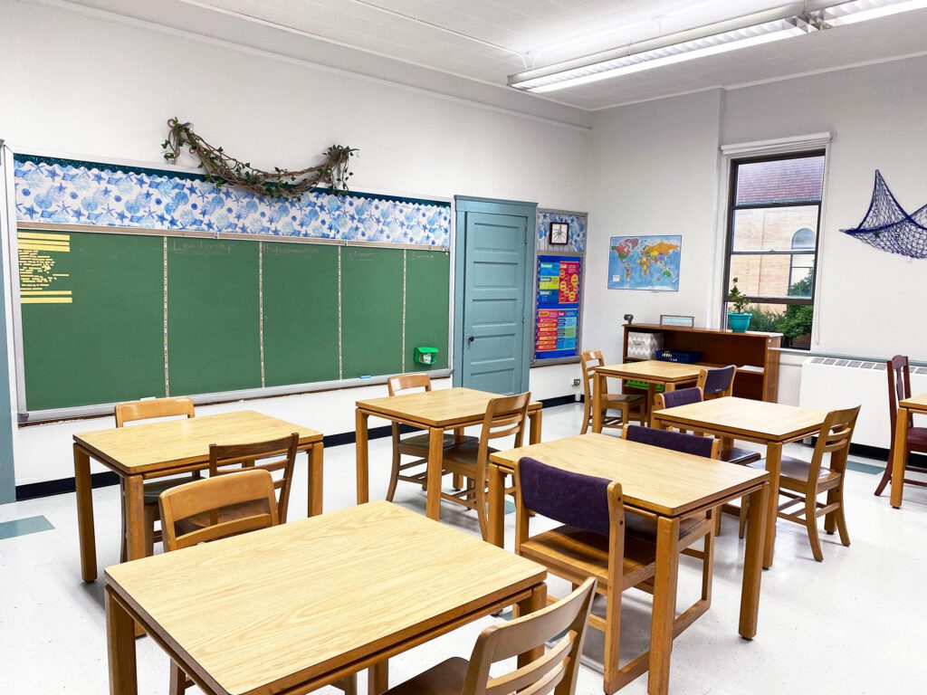 Empty classroom with wooden desks, chairs, and a green chalkboard.