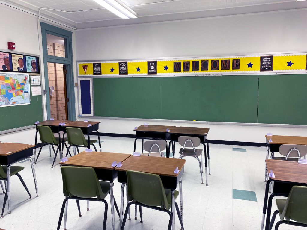 Empty classroom with desks, chairs, and a green chalkboard.