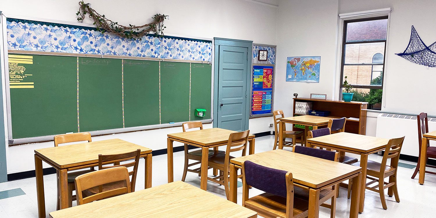 Empty classroom with wooden desks, chairs, and a green chalkboard.