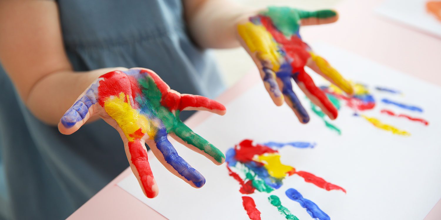 Child's hands covered in colorful paint, making handprints.