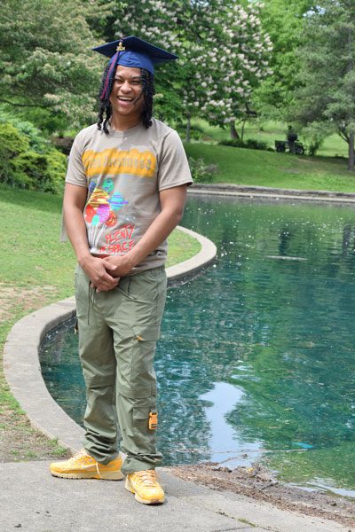 Smiling adult in graduation cap by pond.