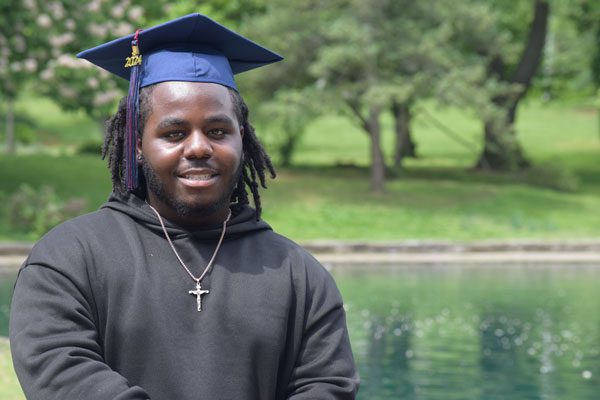 Adult in graduation cap smiles by water.